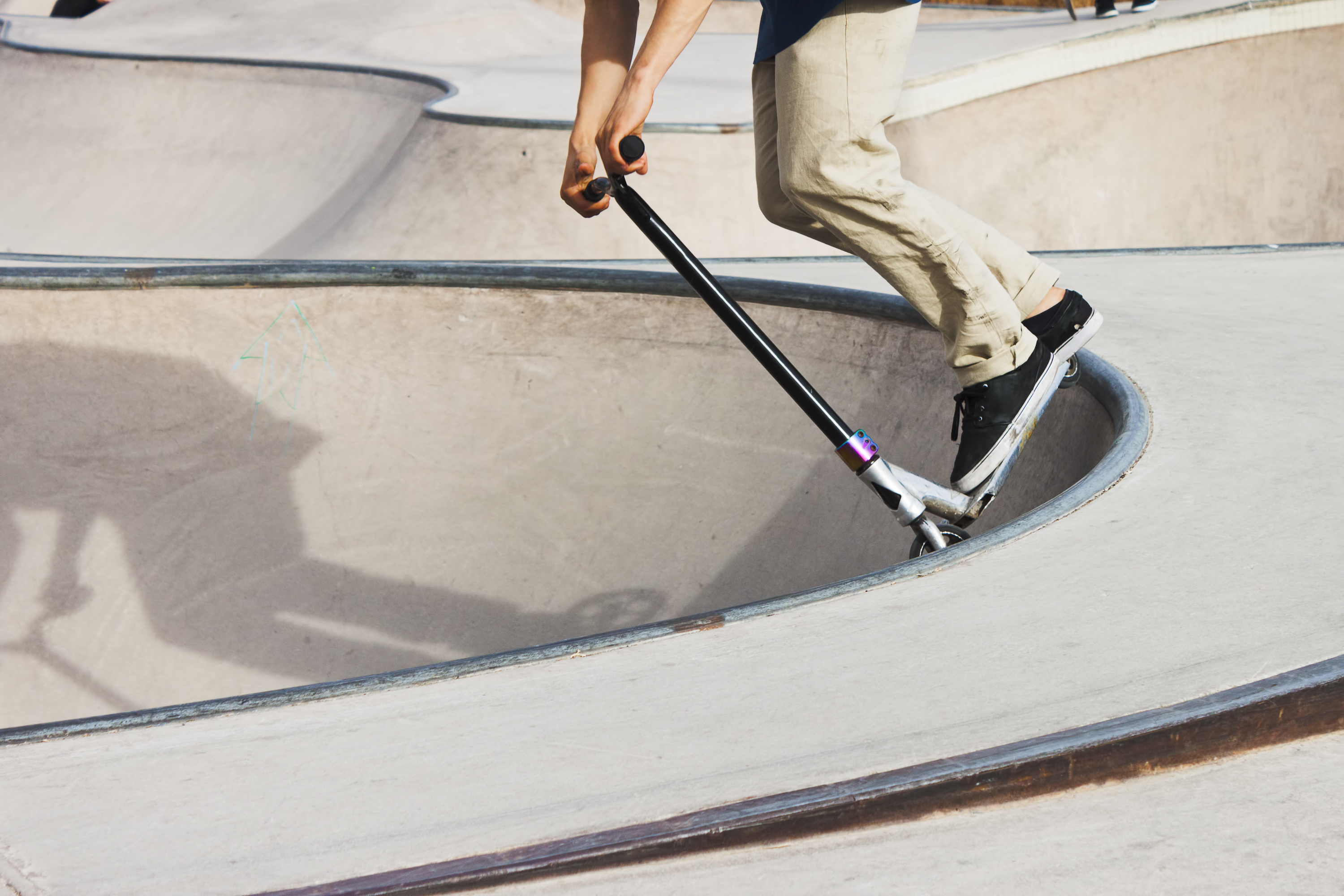 The arms and legs of a boy on a scooter at a skate park.